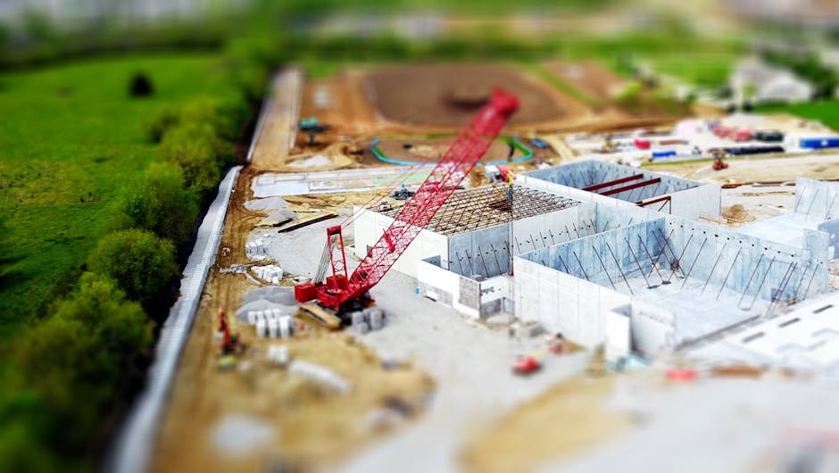 Aerial view of a construction site with a red crane amidst green fields